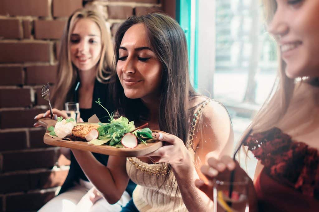 Group of girls having lunch in fashionable restaurant. Smiling young woman enjoying the smell of delicious salad served